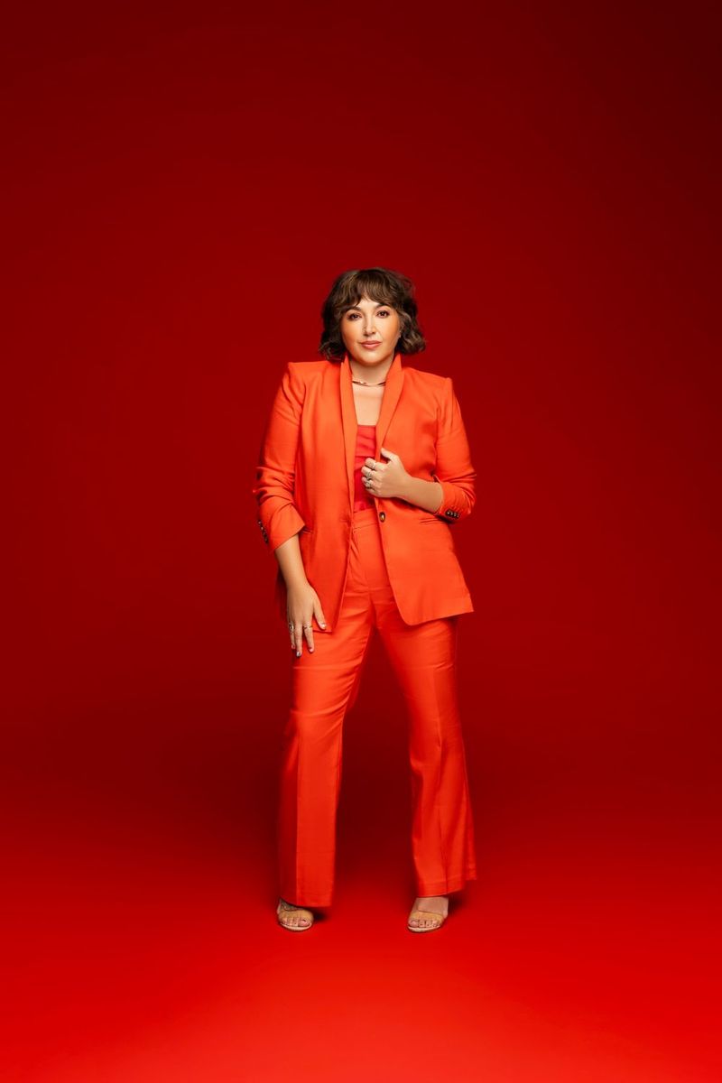 Rachel Dee Minyard, REALTOR® and Creative Director, standing in an orange suit against a red backdrop