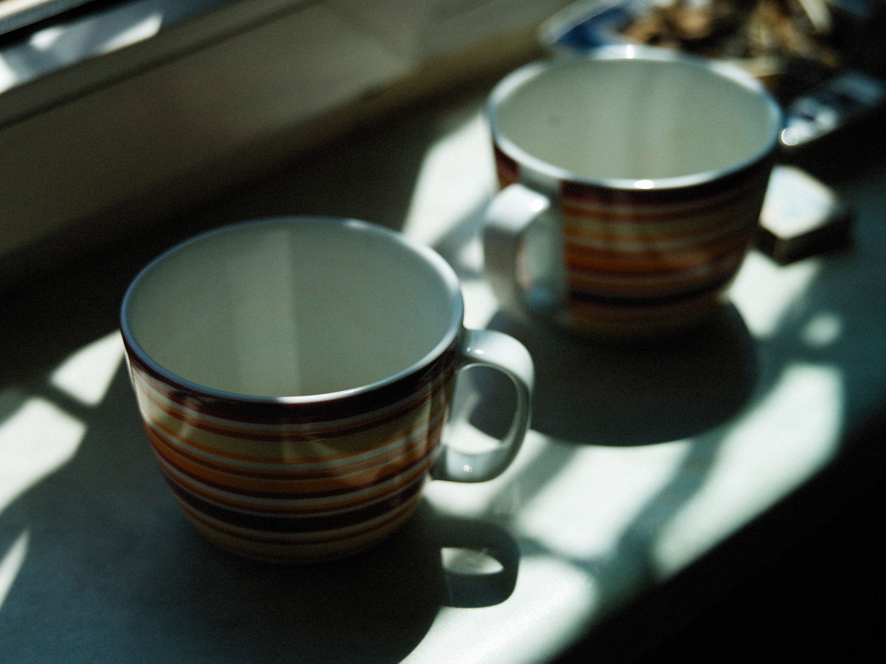 Two striped mugs on a windowsill in morning light and shadow