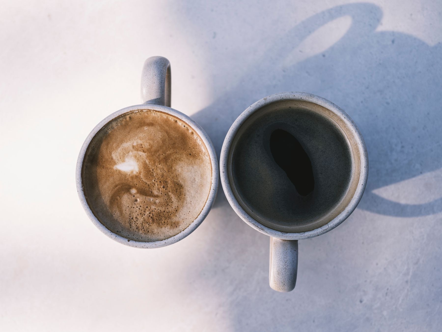 Two coffee mugs side by side on a sunlit table, seen from above