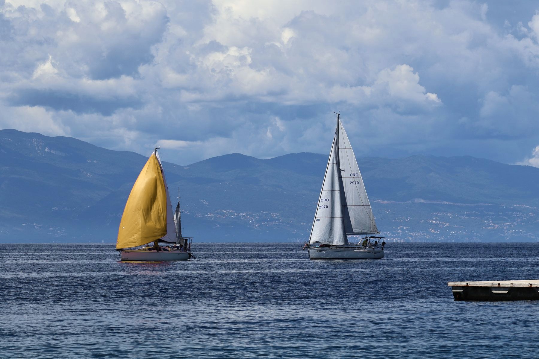 Two sailboats of about the same size on open water, one with a gold sail and one with a white sail