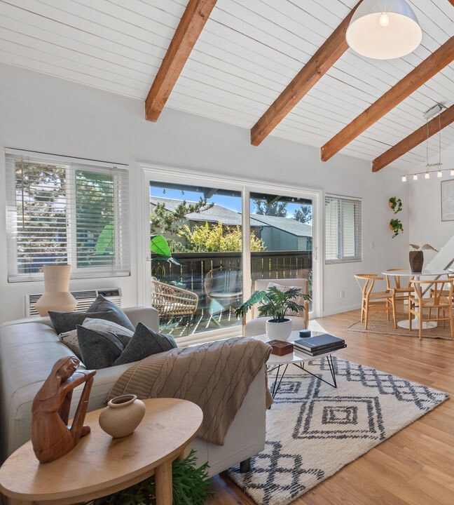 A bright living room with a vaulted ceiling, wood beams and a dining nook