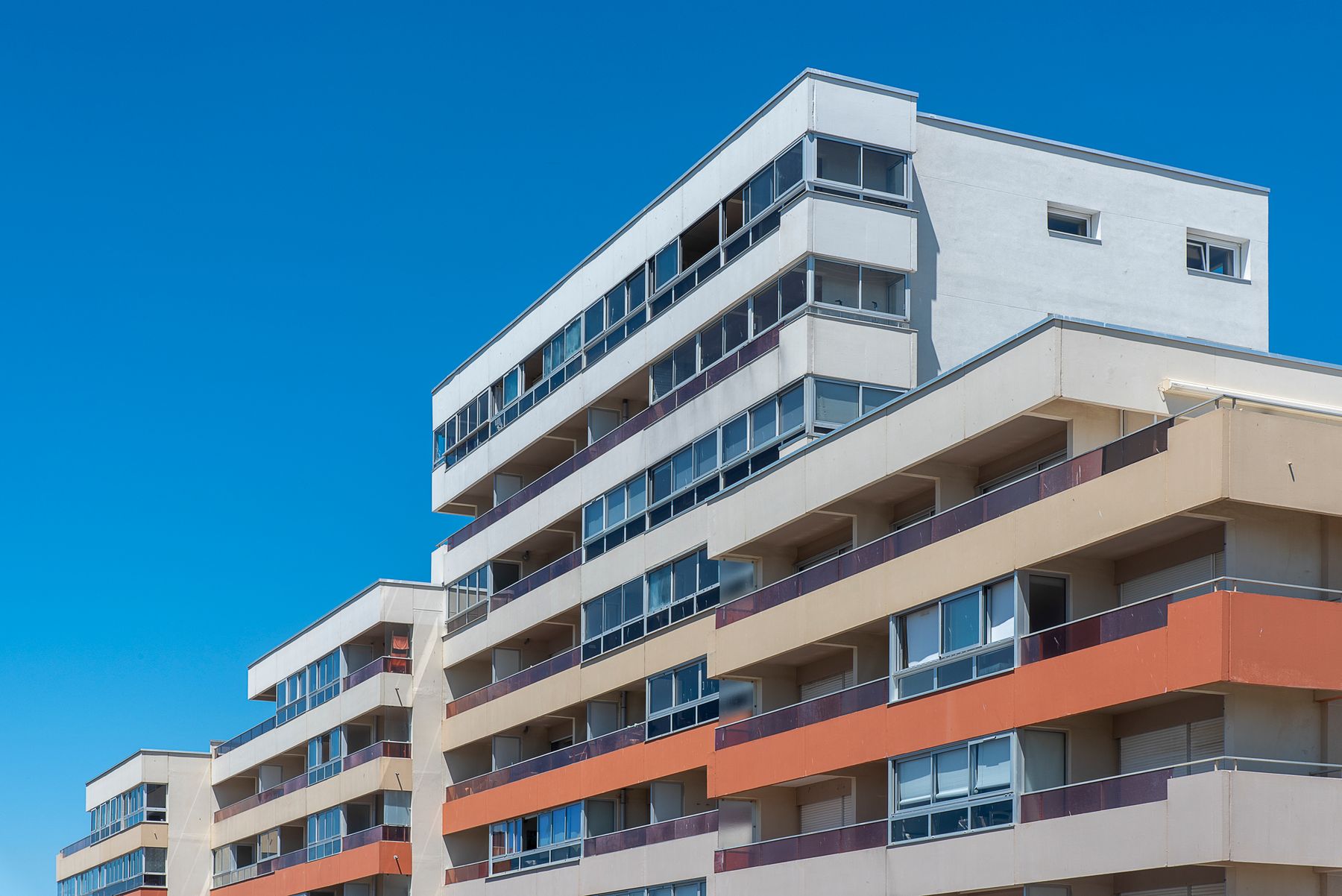 A modern white and terracotta apartment building with balconies against a clear blue sky