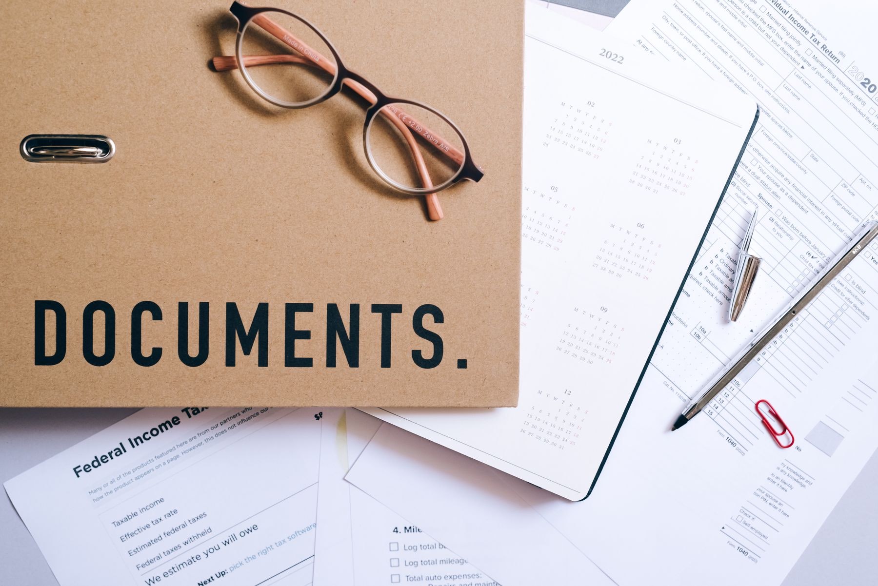 A folder of documents, reading glasses and a calendar on a desk