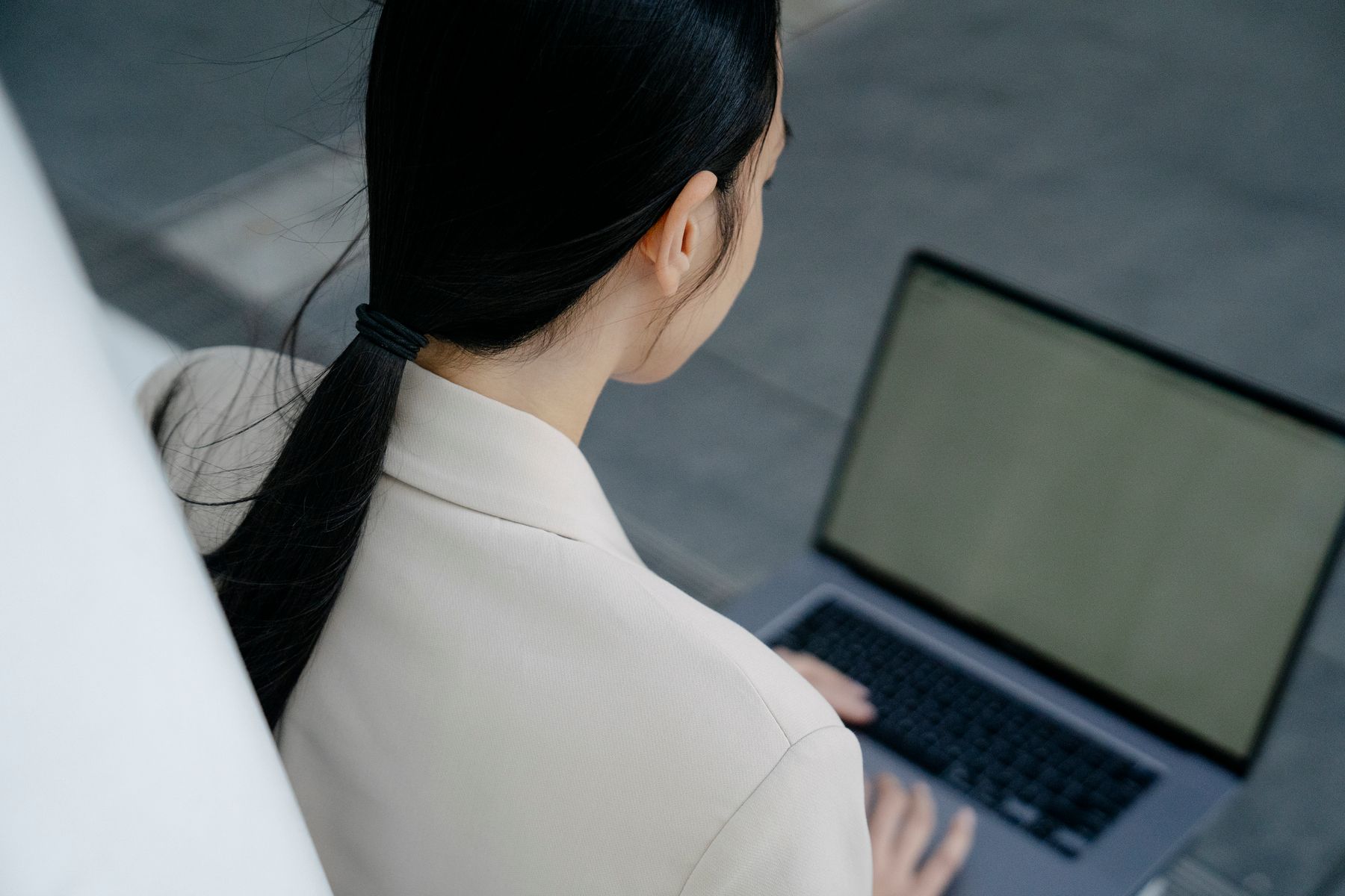 A professional in a cream blazer working on a laptop, seen from behind