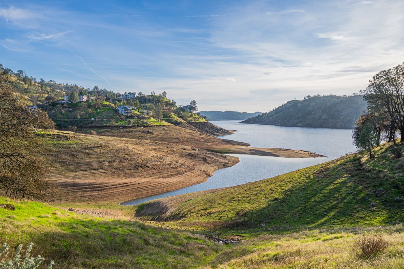 A calm lake among green and gold oak-covered foothills