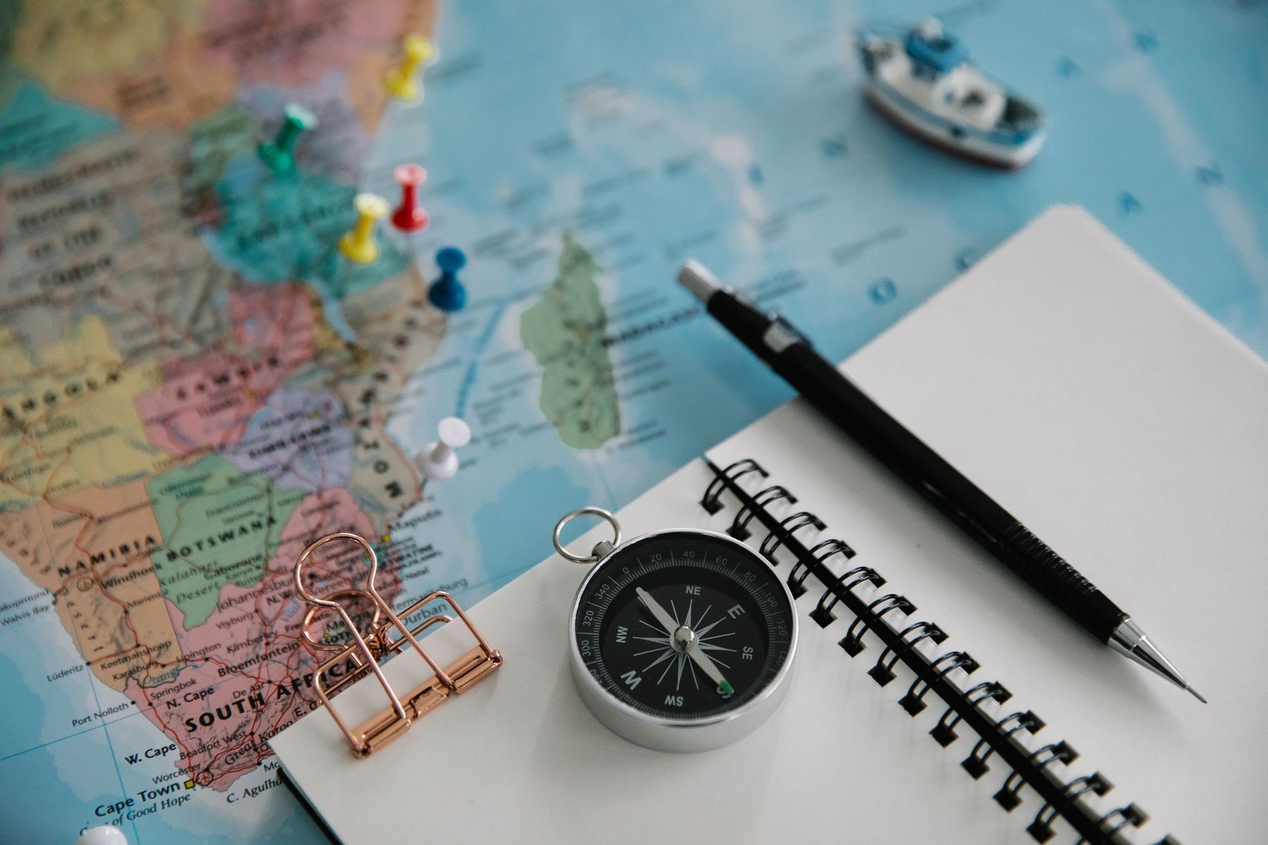 A pinned paper map, a compass, a notebook and a pencil on a table