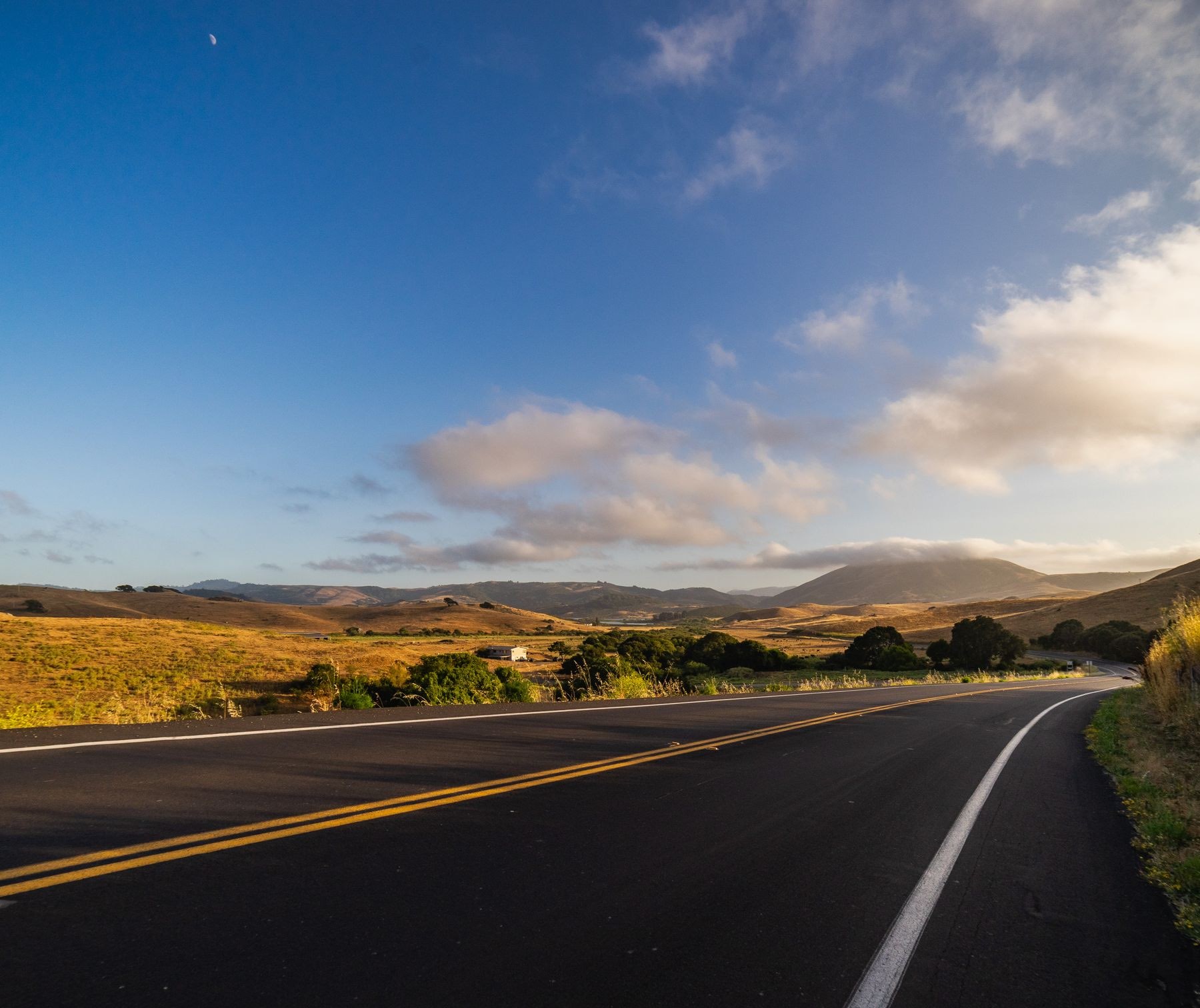 An empty road curving toward golden hills under a blue sky