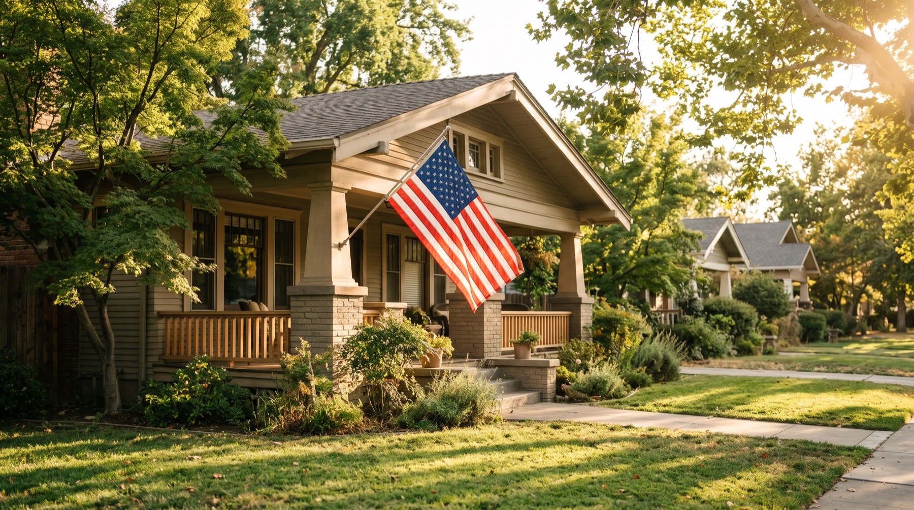 An American flag hanging from the porch of a craftsman home on a tree-lined street